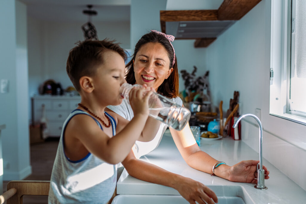 kid drinking water from the tap as his mother watches